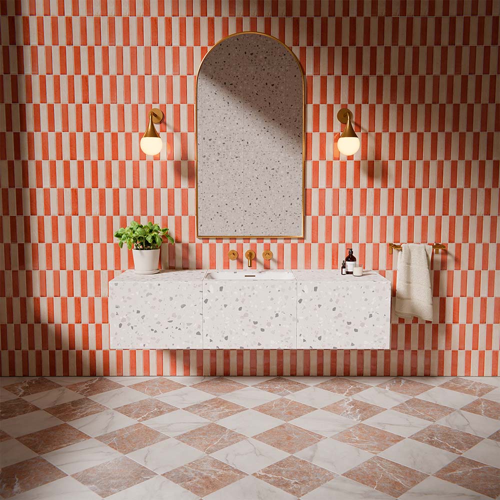 Badezimmer mit der Vitoria Kollektion, mit vertikal gestreiften Wandfliesen in warmen Korall- und Weißtönen, kombiniert mit Schachbrett-Marmorboden, Messingarmaturen und Terrazzo-Waschtisch für ein markantes, designorientiertes Gesamtbild.