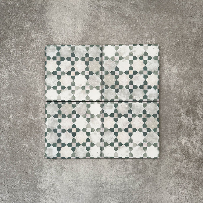 Vier Berber Mequinez Grün Feinsteinzeugfliesen im marokkanischen Stil im Format 15 × 15 cm, gemeinsam angeordnet, um das sanfte geometrische Muster in Grün und Creme auf neutralem Hintergrund hervorzuheben.