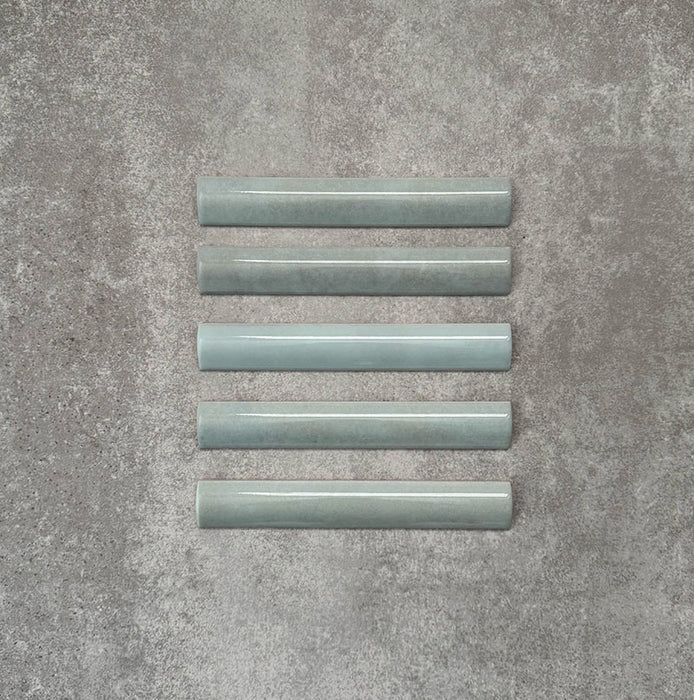 Flatlay mit Zellige Aquablau Bullnose-Keramikfliesen im marokkanischen Stil im Format 3 × 20 cm, die das abgerundete Kantenprofil, die glänzende blau-grüne Glasur und die feine tonale Variation vor neutralem Hintergrund zeigen.