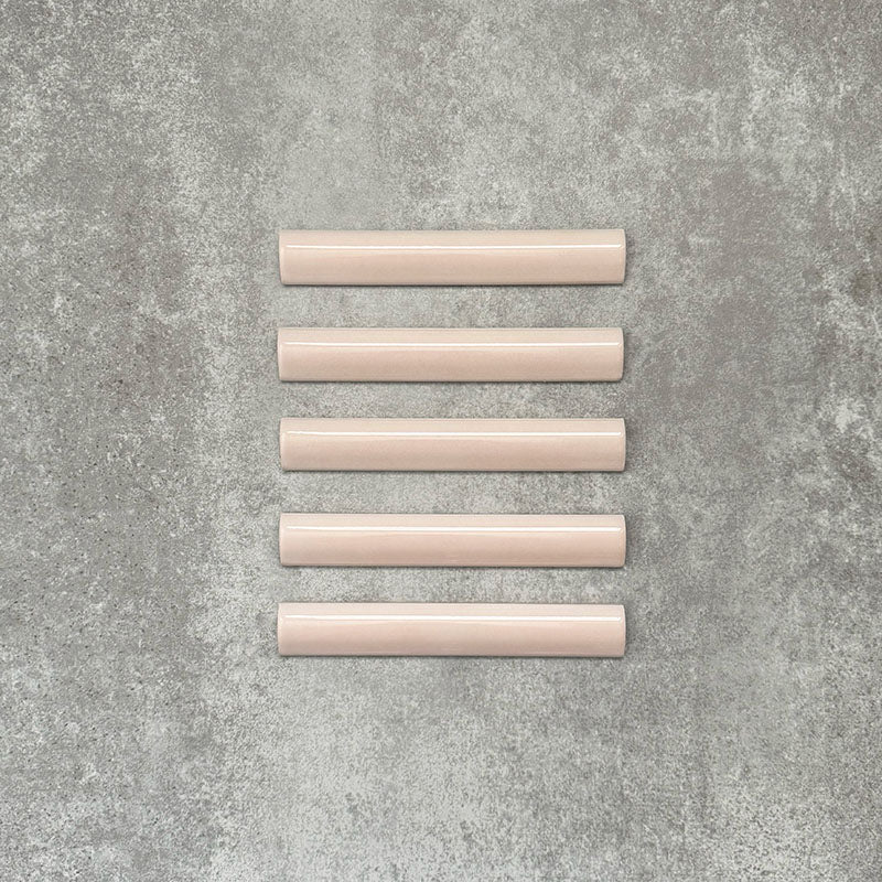 Flatlay mit Zellige Rosa Nebel Bullnose Keramik-Abschlussfliesen im marokkanischen Stil im Format 3 × 20 cm, in sanften, hellen Rosétönen. Die glatte, abgerundete Kante und die glänzende Glasur sind auf einem strukturierten grauen Hintergrund arrangiert und heben die handgefertigte Zellige-Optik sowie das dekorative Abschlussprofil hervor.