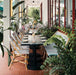 Restaurantterrasse mit Atlas Terrakotta Mini Brick Matt Wand- und Bodenfliesen im Format 5 × 15 cm, kombiniert mit Sitzmöbeln aus Rattan, üppigem Grün und gestreiften Markisen für einen warmen, mediterran inspirierten Außenbereich.