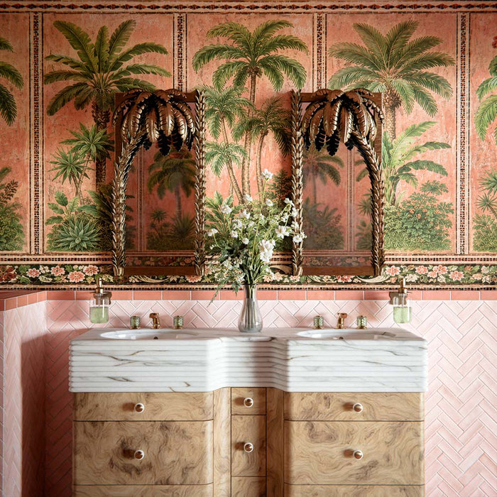 Badezimmer mit Atlas Pink Moroccan Mini Brick Matt Wandfliesen im Format 5 × 15 cm im Fischgrätmuster, kombiniert mit tropischer Palmentapete, geschnitzten Holzspiegeln und Waschbecken in Marmoroptik für ein luxuriöses, eklektisches Interior.