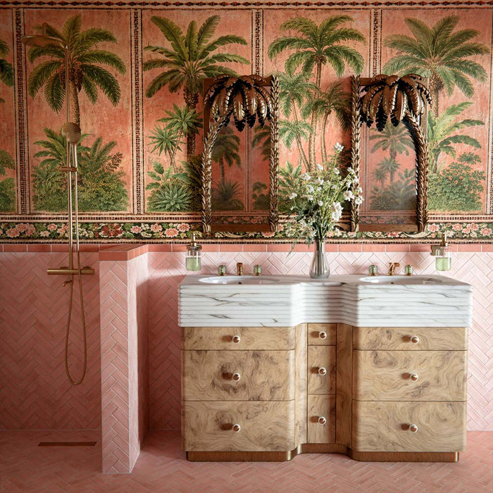 Badezimmer mit Atlas Pink Moroccan Mini Brick Matt Wandfliesen im Format 5 × 15 cm im Fischgrätmuster, kombiniert mit tropischer Palmentapete, geschnitzten Holzspiegeln und Waschbecken in Marmoroptik für ein luxuriöses, eklektisches Interior.