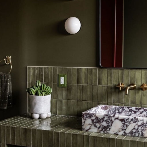 Badezimmer mit Atlas Verde Mini Brick Gloss glänzenden Wandfliesen im Format 5 × 15 cm, kombiniert mit tiefen Olivtönen, Armaturen in Messingoptik und einem Waschbecken in Marmoroptik für ein modernes und elegantes Badezimmerdesign.