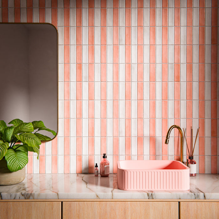 Badezimmer mit Atlas White Mini Brick Gloss glänzenden Wandfliesen im Format 5 × 15 cm im Streifenlayout, kombiniert mit einem Waschbecken in Blush-Pink, einer Waschtischplatte in Marmoroptik und Armaturen in Messingoptik für ein verspieltes, modernes Interior.