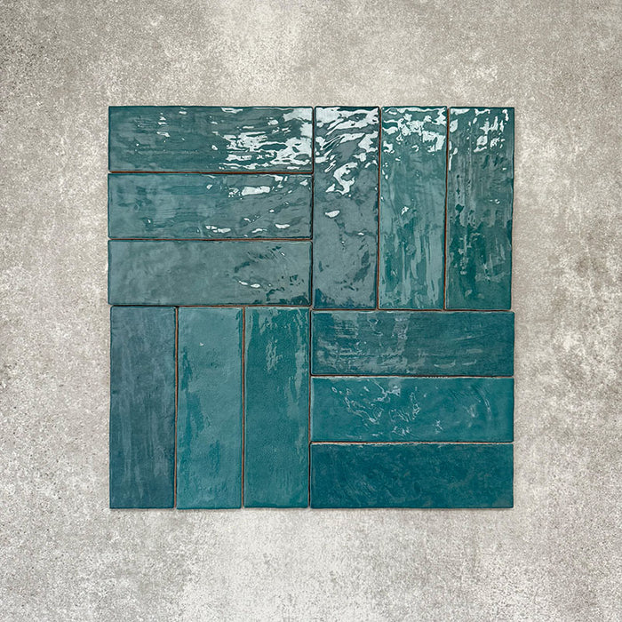 Flatlay von Zellige Pfauengrün Keramik-Ziegelfliesen im marokkanischen Stil im Format 6,5 × 20 cm, im Flechtmuster angeordnet. Die tiefen Blau-Grün-Töne, die glänzende Glasur und die natürliche Farbvariation werden auf neutralem Hintergrund besonders hervorgehoben.