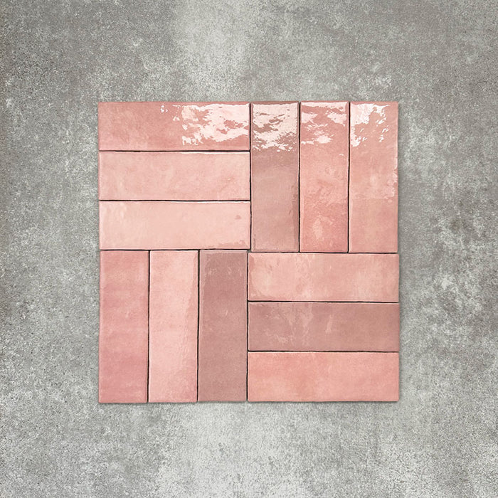 Flatlay von Zellige Rosa Brick Keramikfliesen im marokkanischen Stil im Format 6,5 × 20 cm, in sanften Blush-, Altrosa- und Terrakotta-Pinktönen mit feiner Farbvariation und leicht unregelmäßigen Kanten. Im Flechtmuster (Basketweave) auf strukturiertem grauem Hintergrund arrangiert, um die handwerkliche Zellige-Optik zu zeigen.