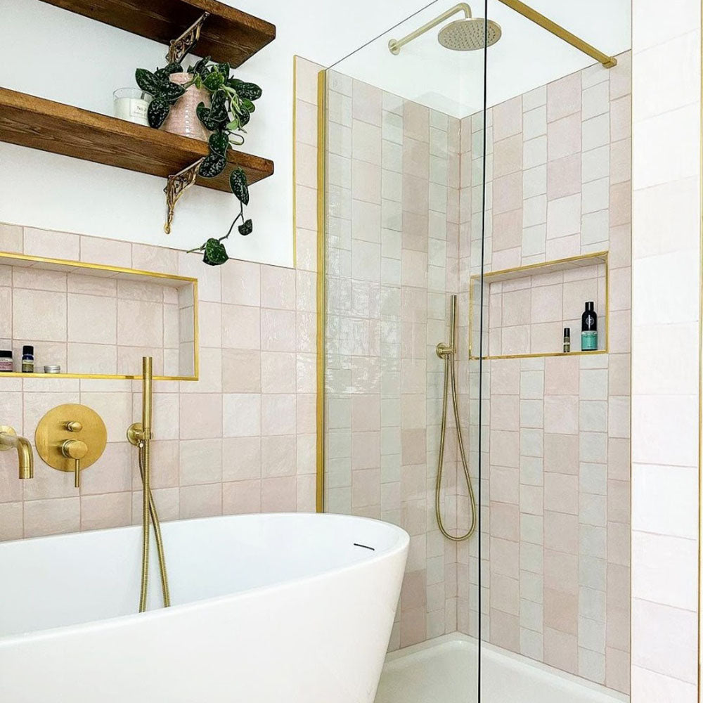 Badezimmer mit Zellige Rosa Nebel Quadrat Keramik-Wandfliesen im marokkanischen Stil im Format 13,2 × 13,2 cm, in sanften, hellen Rosétönen. In einem sauberen Raster rund um eine freistehende Badewanne und eine bodengleiche Dusche verlegt und kombiniert mit Messingarmaturen, Glasabtrennungen und offenen Regalen entsteht ein ruhiges, elegantes Finish mit Zellige-Effekt.
