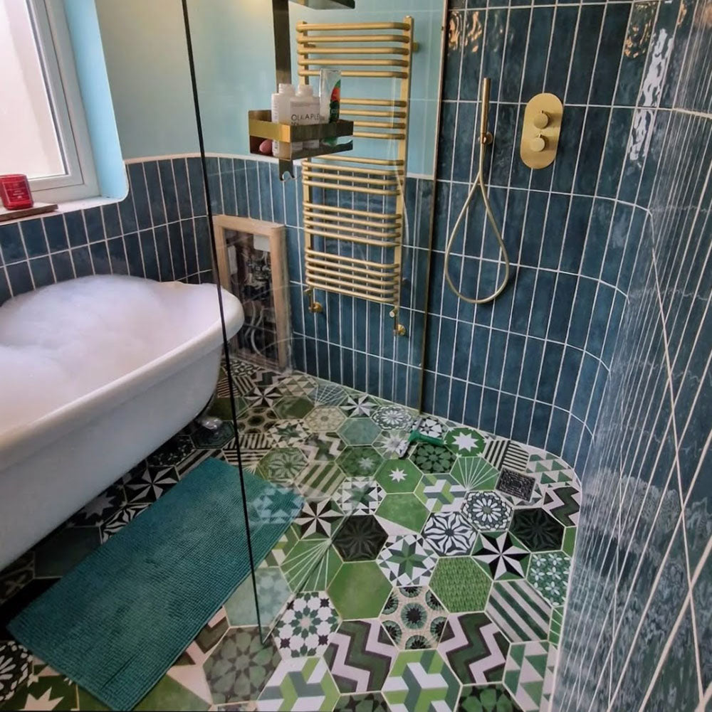 Badezimmer mit Fayrouz Verde Hexagon Patchwork Feinsteinzeugfliesen im marokkanischen Stil im Hexagonformat 18,7 × 21,6 cm. Die Kombination aus filigranen geometrischen und sternförmigen Mustern in abgestuften Grün-, Salbei- und Anthrazittönen wird mit tiefblauen glasierten Wandfliesen, Armaturen in gebürsteter Messingoptik und einer geschwungenen Walk-in-Dusche ergänzt und schafft ein ausdrucksstarkes, charaktervolles Gesamtbild.
