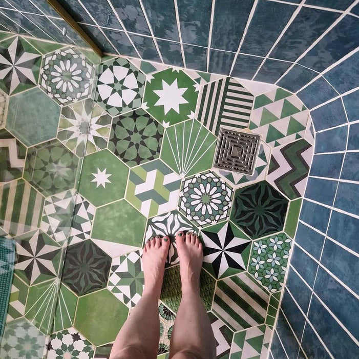 Badezimmer mit Fayrouz Verde Hexagon Patchwork Feinsteinzeugfliesen im marokkanischen Stil im Hexagonformat 18,7 × 21,6 cm. Die Kombination aus filigranen geometrischen und sternförmigen Mustern in abgestuften Grün-, Salbei- und Anthrazittönen wird mit tiefblauen glasierten Wandfliesen, Armaturen in gebürsteter Messingoptik und einer geschwungenen Walk-in-Dusche ergänzt und schafft ein ausdrucksstarkes, charaktervolles Gesamtbild.
