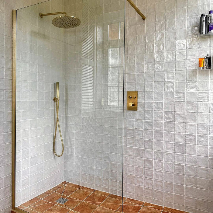 Begehbare Dusche mit Zellige Auster Quadrat Keramikfliesen im marokkanischen Stil im Format 10 × 10 cm, gleichmäßig im Raster verlegt. Die glänzende Auster-Weiß-Glasur, sanft unebene Oberflächen und feine Farbnuancen werden durch gebürstete Messingarmaturen und eine Glasabtrennung ergänzt und schaffen ein warmes Bad mit handwerklicher Anmutung.