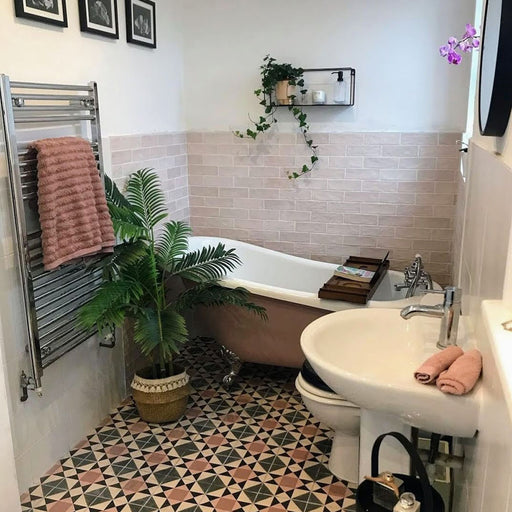 Badezimmer mit Zellige Rosa Nebel Ziegel Keramik-Wandfliesen im marokkanischen Stil im Format 6,5 × 20 cm, in sanften, hellen Rosétönen. Horizontal im Ziegelverband rund um eine freistehende Badewanne verlegt und kombiniert mit geometrisch gemusterten Bodenfliesen, weißer Keramik und botanischen Akzenten entsteht ein ruhiges, charaktervolles Finish mit Zellige-Effekt.