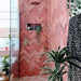 Badezimmerwand mit Zellige Rosa Brick Keramikfliesen im marokkanischen Stil im Format 6,5 × 20 cm, im Fischgrätmuster verlegt. Sanfte Blush- und Pudertöne in Rosa werden mit Wand- und Armaturen in Messing, einer grün gestrichenen Tür und einem Spiegel mit Rundbogen kombiniert – für ein warmes, charaktervolles Finish mit handgefertigter Zellige-Optik.