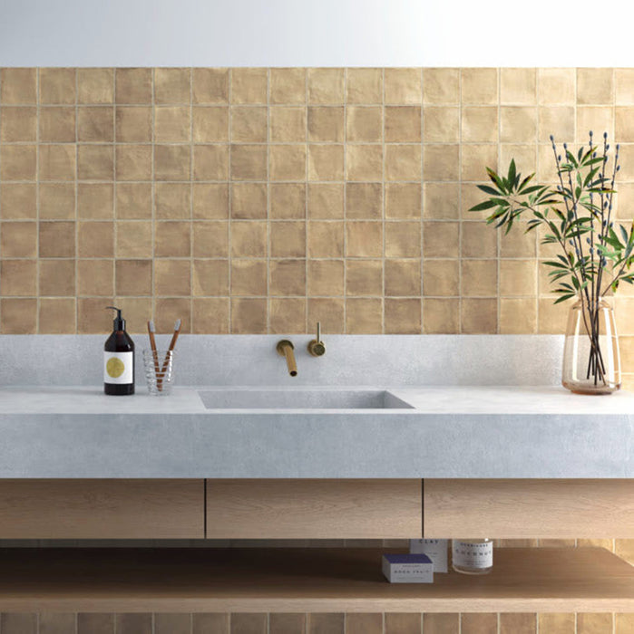 Badezimmer-Spritzschutz mit Zellige Sandbeige Matt Quadrat Keramik-Wandfliesen im marokkanischen Stil im Format 10 × 10 cm, in warmen Beigetönen. Sauber im Raster oberhalb eines Waschtischs in Betonoptik mit wandmontierten Messingarmaturen verlegt, sorgen feine Farbvariationen und sanft unregelmäßige Kanten für eine authentische Zellige-Optik.