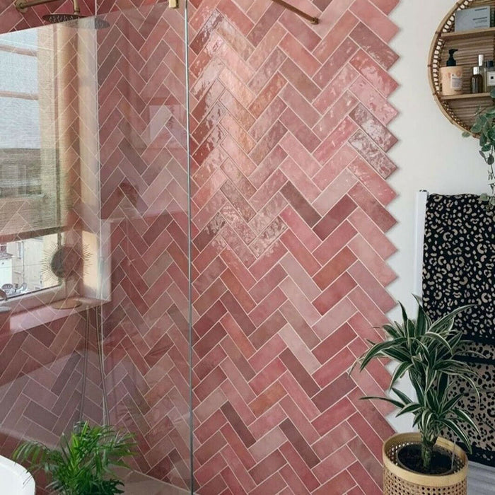 Badezimmerwand mit Zellige Rosa Brick Keramikfliesen im marokkanischen Stil im Format 6,5 × 20 cm, im Fischgrätmuster verlegt. Sanfte Blush- und Pudertöne in Rosa werden mit Wand- und Armaturen in Messing, einer grün gestrichenen Tür und einem Spiegel mit Rundbogen kombiniert – für ein warmes, charaktervolles Finish mit handgefertigter Zellige-Optik.