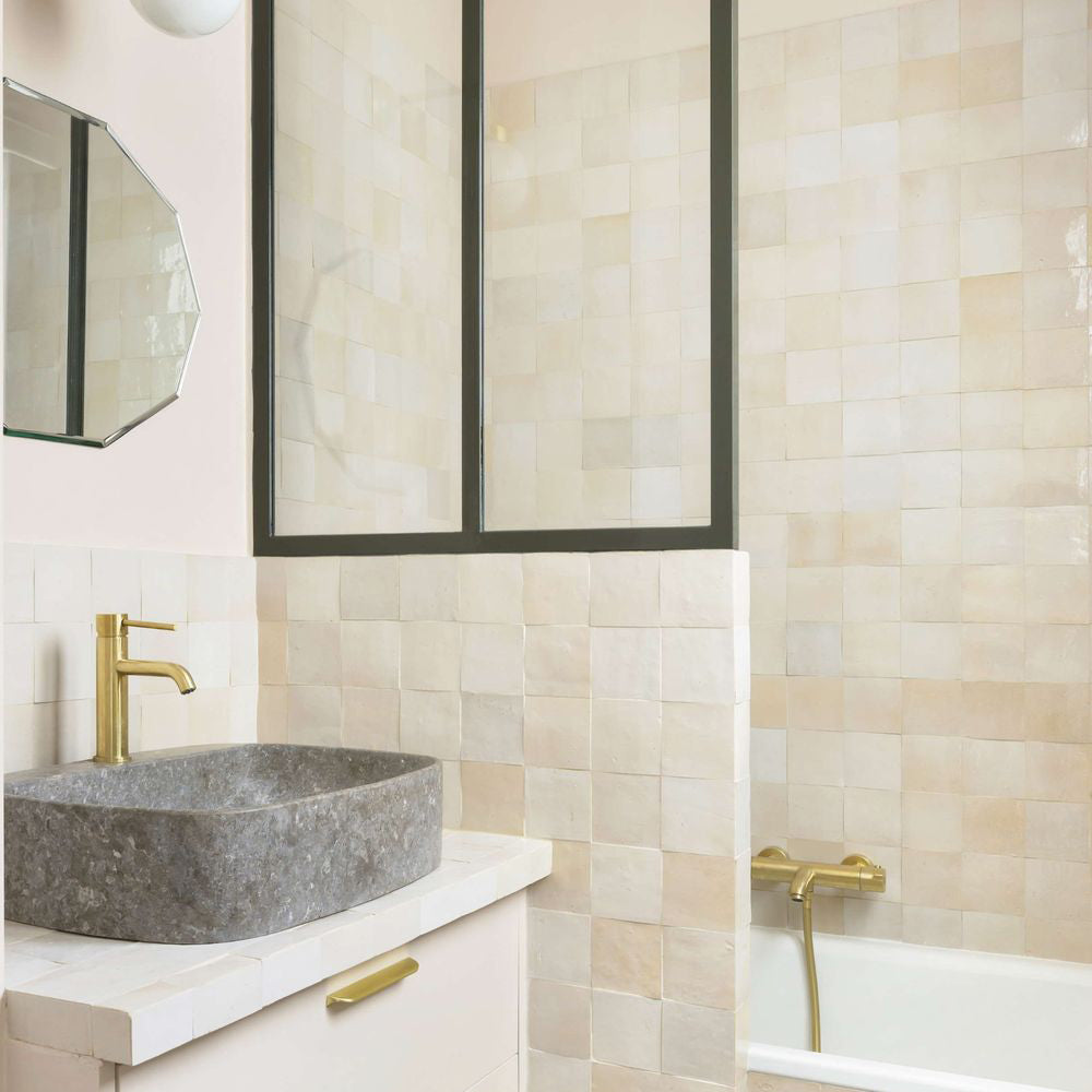 Badezimmer mit Zellige Beige quadratischen Fliesen im marokkanischen Stil in sanften, neutralen Tönen, kombiniert mit Armaturen in Messing und einem Waschbecken aus Stein.