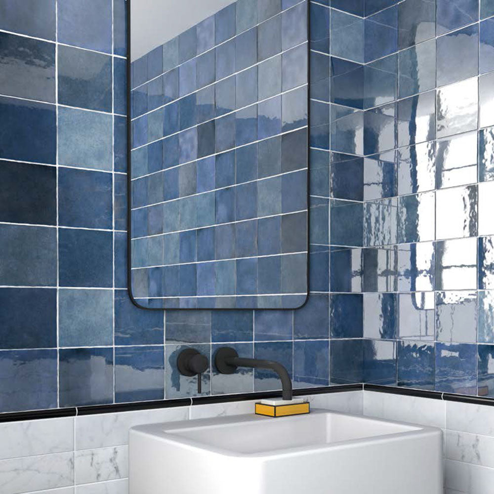 Badezimmer mit Zellige Königliches Blau Keramik-Quadratfliesen im marokkanischen Stil im Format 13,2 × 13,2 cm, an den Wänden verlegt. Die satten Blautöne mit glänzender Glasur in handgefertigter Optik werden kombiniert mit mattschwarzen Armaturen, einem minimalistischen Waschtisch und einem modernen Spiegel.