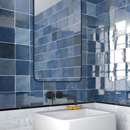 Badezimmer mit Zellige Königliches Blau Keramik-Quadratfliesen im marokkanischen Stil im Format 13,2 × 13,2 cm, an den Wänden verlegt. Die satten Blautöne mit glänzender Glasur in handgefertigter Optik werden kombiniert mit mattschwarzen Armaturen, einem minimalistischen Waschtisch und einem modernen Spiegel.