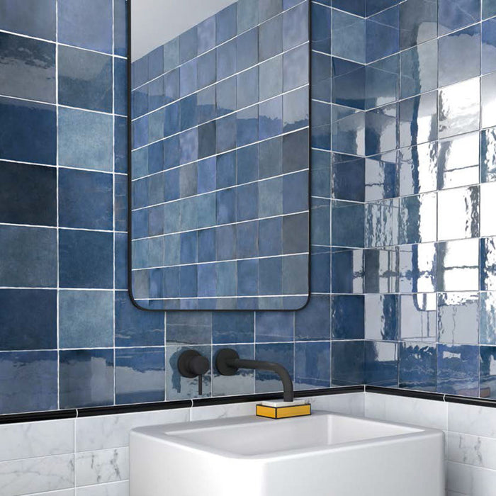 Badezimmer mit Zellige Königliches Blau Keramik-Quadratfliesen im marokkanischen Stil im Format 13,2 × 13,2 cm, an den Wänden verlegt. Die satten Blautöne mit glänzender Glasur in handgefertigter Optik werden kombiniert mit mattschwarzen Armaturen, einem minimalistischen Waschtisch und einem modernen Spiegel.