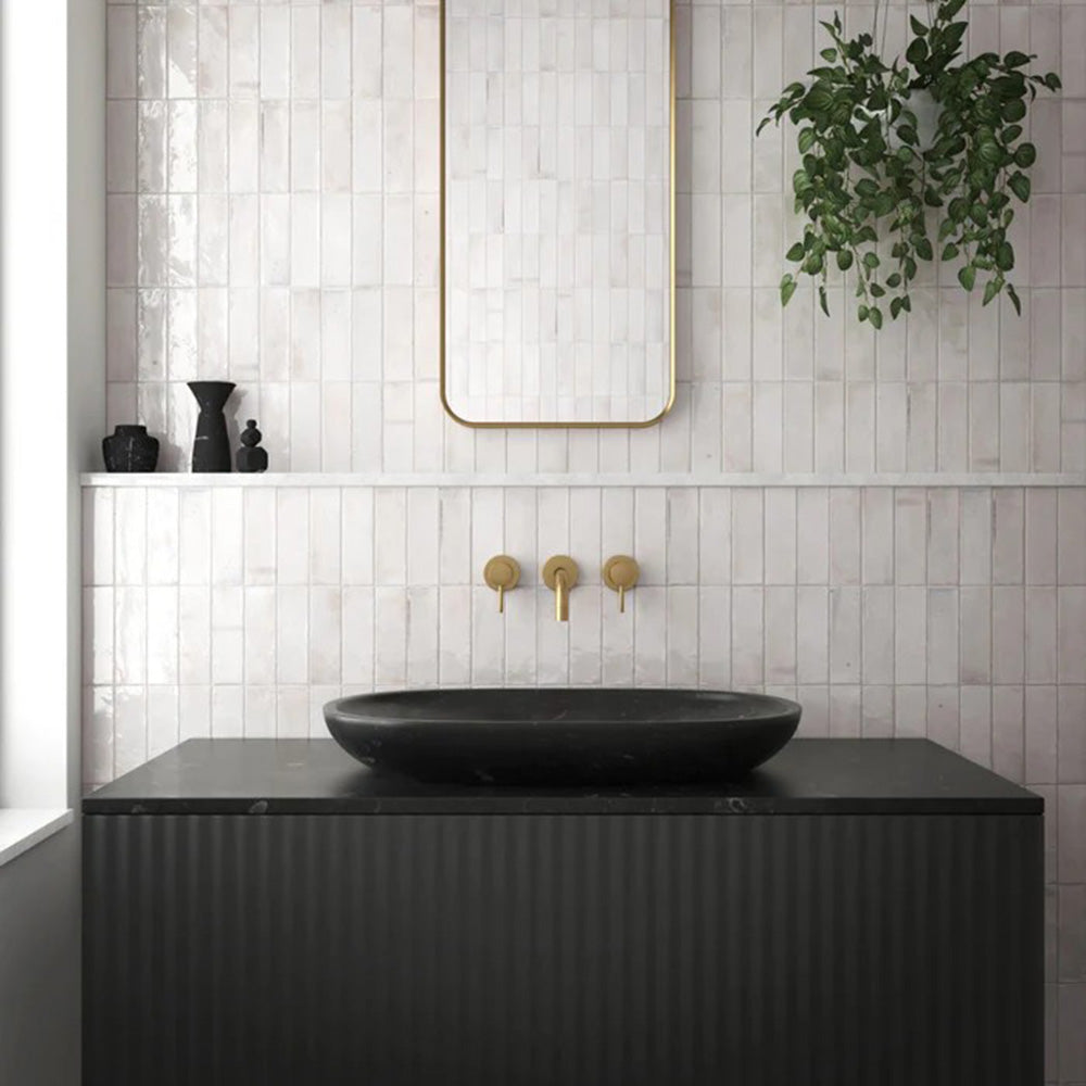 Badezimmerwand mit Saigon Weiß Brick Wandfliesen im marokkanisch inspirierten Stil. Glänzende Keramikfliesen im Format 5,1 × 16,1 cm in sanften Weißtönen, kombiniert mit einem schwarzen Waschtisch, Messingarmaturen und einem minimalistischen Spiegel.