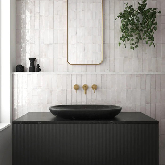 Badezimmerwand mit Saigon Weiß Brick Wandfliesen im marokkanisch inspirierten Stil. Glänzende Keramikfliesen im Format 5,1 × 16,1 cm in sanften Weißtönen, kombiniert mit einem schwarzen Waschtisch, Messingarmaturen und einem minimalistischen Spiegel.