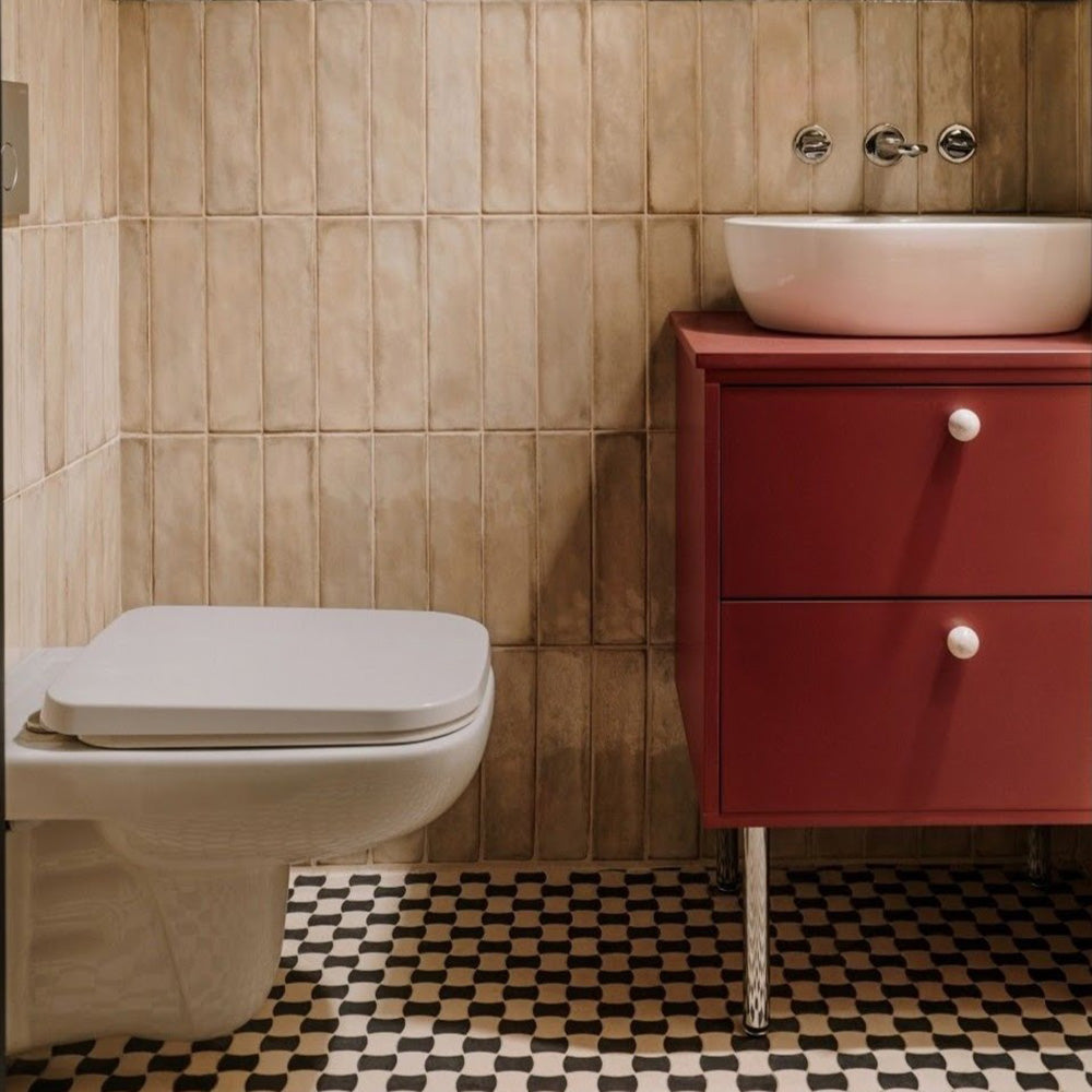 Badezimmer mit Zellige Sandbeige Matt Ziegel Keramik-Wandfliesen im marokkanischen Stil im Format 6,5 × 20 cm, in warmen Beigetönen. Vertikal im Ziegelverband hinter einem wandhängenden WC und einem roten Waschtischunterschrank verlegt, kombiniert mit gemusterten Bodenfliesen in Schwarz und Creme sowie Chromarmaturen für ein modernes, charaktervolles Finish.
