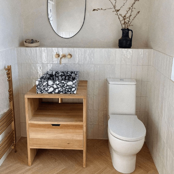 Badezimmer mit Zellige Auster Brick Keramik-Wandfliesen im marokkanischen Stil im Format 6,5 × 20 cm, vertikal verlegt, um halbhohe, strukturierte Wandflächen zu schaffen. Kombiniert mit einem Aufsatzwaschbecken in Terrazzo-Optik, einem Waschtisch aus warmem Holz und Messingarmaturen entsteht ein sanftes, modernes Badkonzept.