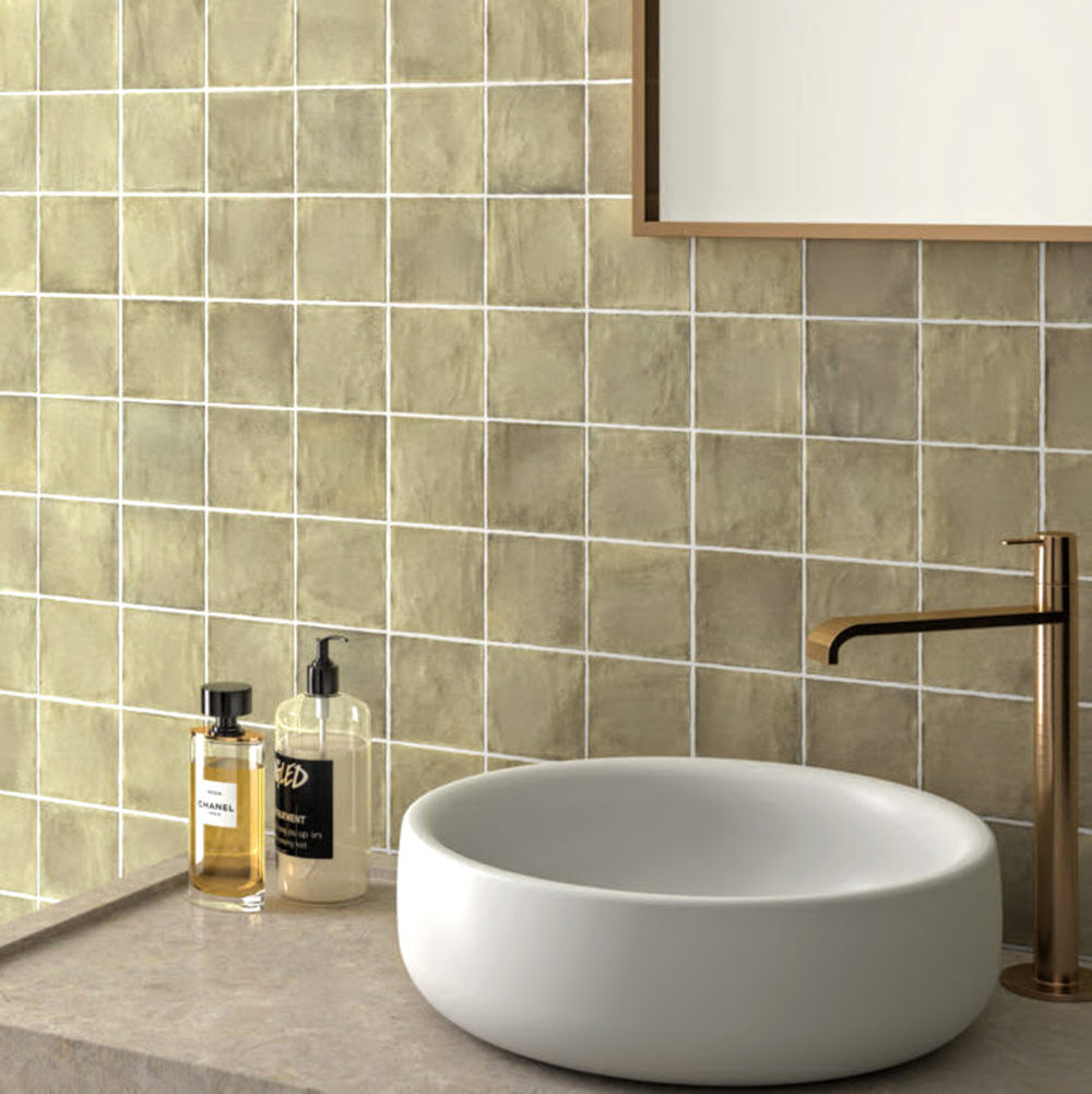 Badezimmer mit Zellige Waldgrün Matt Keramik-Quadratfliesen im marokkanischen Stil im Format 10 × 10 cm, hinter dem Waschtisch an der Wand verlegt. Die sanfte grüne Farbvariation und die handgefertigte Optik werden durch eine Naturstein-Arbeitsplatte, ein rundes Aufsatzwaschbecken und Messingarmaturen ergänzt.