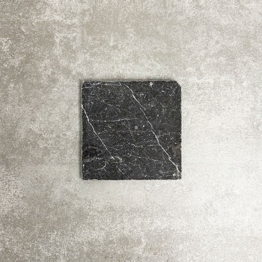 Single Fayrouz Black 15.2x15.2cm natural marble tile with a tumbled finish, featuring deep charcoal tones and striking natural veining, displayed against a neutral textured background in a clean product setting.