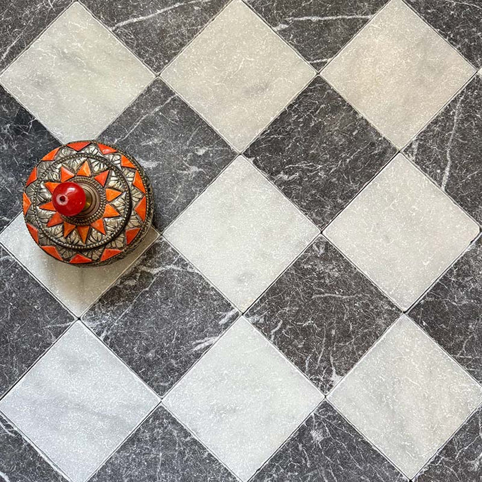 Schachbrettmuster mit Fayrouz Black Naturmarmorfliesen im Format 15,2 × 15,2 cm mit getrommelter Oberfläche, kombiniert mit weißen Marmorfliesen. Diagonal verlegt und mit einer dekorativen, gemusterten Schale in Szene gesetzt, um einen spannenden Kontrast zu schaffen.