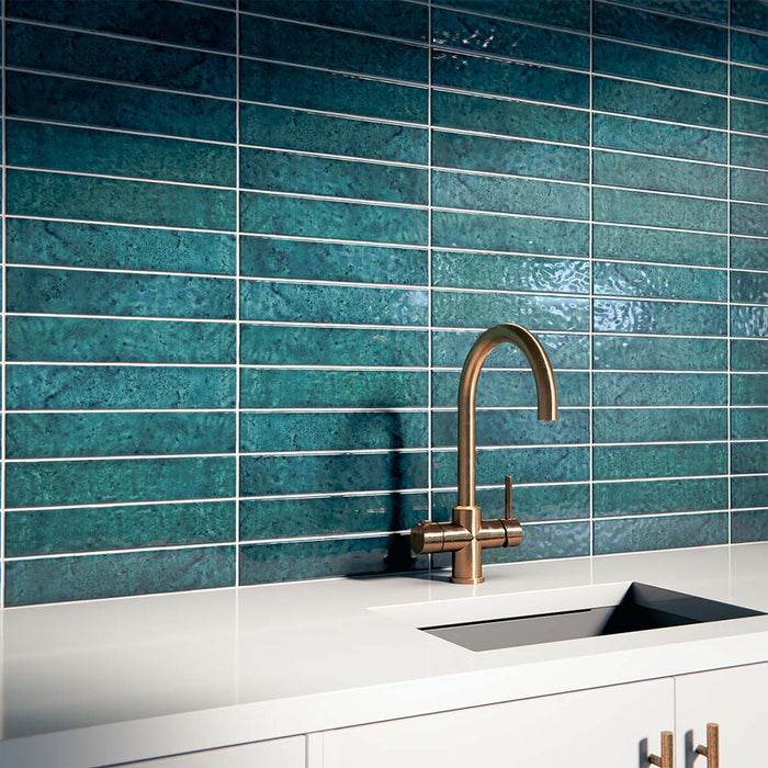 Küchenrückwand mit Bora Bora Brick Amun Blue Wandfliesen im Format 6,5 × 32,8 cm, die die satten blau schimmernden Flux-Glasureffekte zur Geltung bringen. Kombiniert mit einer weißen Arbeitsplatte, einem integrierten Spülbecken und einer Armatur in gebürsteter Messingoptik entsteht ein eleganter und zeitgemäßer Look.