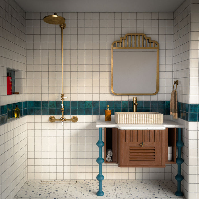 Badezimmer mit Bora Bora Quadrat Weißer Sand Wandfliesen im Format 10 × 10 cm, kombiniert mit einer petrolfarbenen Fliesenbordüre, einem Boden in Terrazzo-Optik, Messingarmaturen und einem Waschtischunterschrank aus Holz.