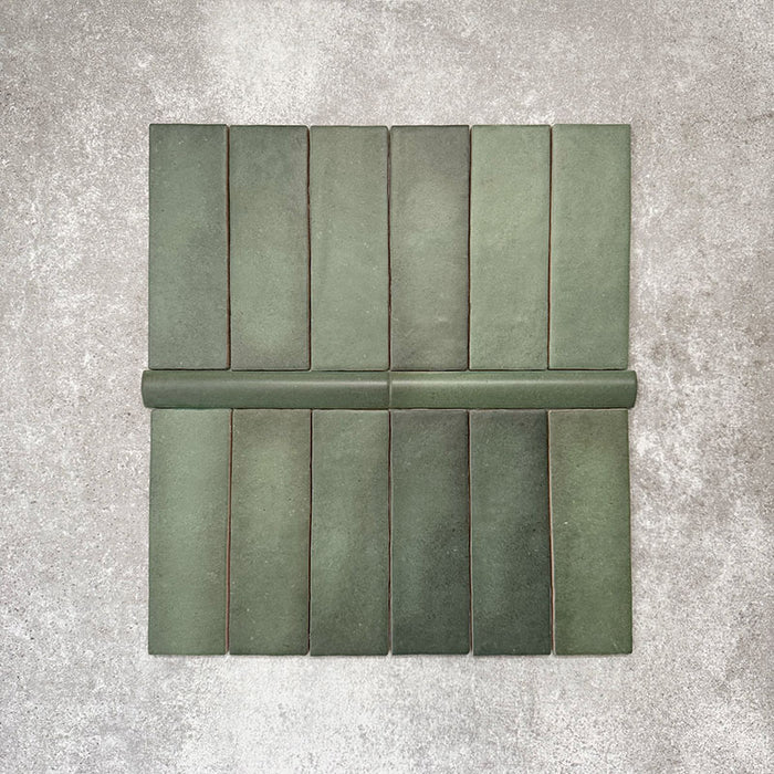 Flatlay mit Zellige Malachitgrün Matt Keramikfliesen im marokkanischen Stil, bestehend aus 6,5 × 20 cm Riemchenfliesen in Kombination mit einer 3 × 20 cm Bullnose-Abschlussfliese. Das Arrangement hebt das abgerundete Kantenprofil, die handwerkliche Oberflächenstruktur und die natürliche grüne Farbvariation hervor.