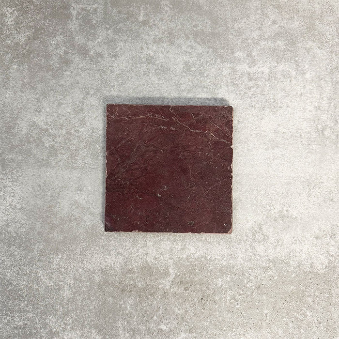 Einzelne Fayrouz Bordeaux 15,2 × 15,2 cm Naturmarmorfliese mit getrommelter Oberfläche in tiefen Rottönen mit natürlicher Maserung, präsentiert vor einem neutralen, strukturierten Hintergrund in einer klaren Produktszene.