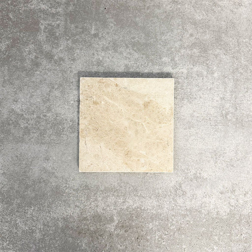 Einzelne Fayrouz Cappuccino 15,2 × 15,2 cm Naturmarmorfliese mit getrommelter Oberfläche in sanften Cremetönen mit feiner natürlicher Maserung, präsentiert vor einem neutralen, strukturierten Hintergrund in einer klaren Produktszene.