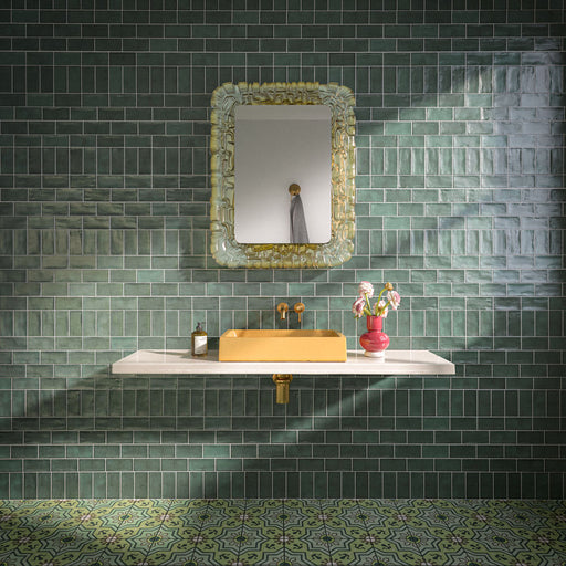 Badezimmer mit Dordogne Grüne Kiefern Rustikale glänzende Wandfliesen im Format 7,5 × 15 cm in satten Grüntönen mit handwerklich inspirierter Farbvariation. Kombiniert mit einem schwebenden Waschtischunterschrank in Weiß, einem senfgelben Waschbecken, Armaturen in Messingoptik, einem verzierten Spiegel und gemusterten grünen Bodenfliesen entsteht ein ausdrucksstarkes und stilvolles Badezimmerdesign.