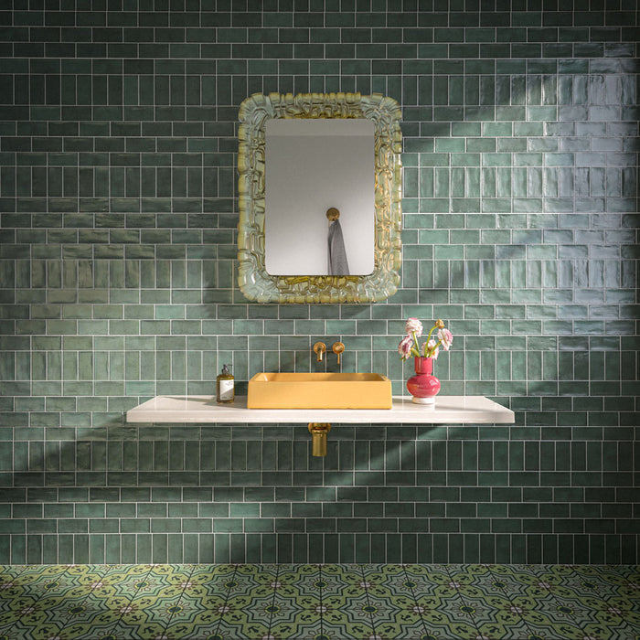 Badezimmer mit Dordogne Grüne Kiefern Rustikale glänzende Wandfliesen im Format 7,5 × 15 cm in satten Grüntönen mit handwerklich inspirierter Farbvariation. Kombiniert mit einem schwebenden Waschtischunterschrank in Weiß, einem senfgelben Waschbecken, Armaturen in Messingoptik, einem verzierten Spiegel und gemusterten grünen Bodenfliesen entsteht ein ausdrucksstarkes und stilvolles Badezimmerdesign.