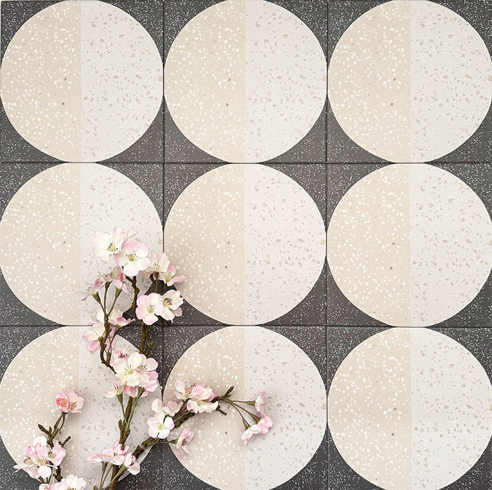 Nahaufnahme der Eclipse Lunar Dekorfliesen im Terrazzo-Look im Format 20 × 20 cm in sanften Creme- und Anthrazittönen, mit geometrischen Kreisdesigns und gesprenkelten Details, kombiniert mit zarten rosa floralen Akzenten.