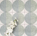 Close-up of Eclipse Salvia 20x20cm terrazzo-effect decorative tiles in soft sage and grey tones, featuring geometric circular patterns with speckled detailing, styled with white floral accents.