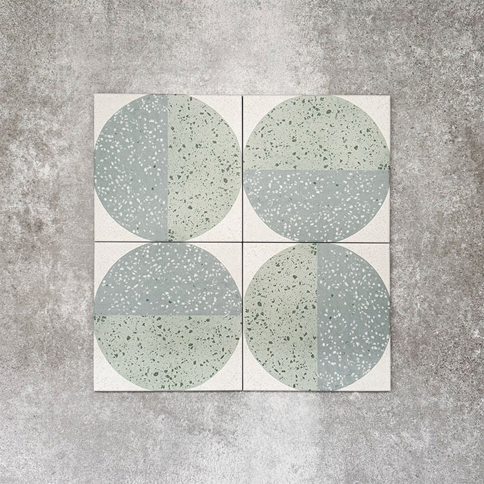Produktpräsentation der Eclipse Salvia Dekorfliesen im Terrazzo-Look im Format 20 × 20 cm in sanften Salbei- und Grautönen, mit geometrischen Kreisdesigns und gesprenkelten Details vor einem Hintergrund in strukturierter Betonoptik.