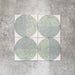 Produktpräsentation der Eclipse Salvia Dekorfliesen im Terrazzo-Look im Format 20 × 20 cm in sanften Salbei- und Grautönen, mit geometrischen Kreisdesigns und gesprenkelten Details vor einem Hintergrund in strukturierter Betonoptik.