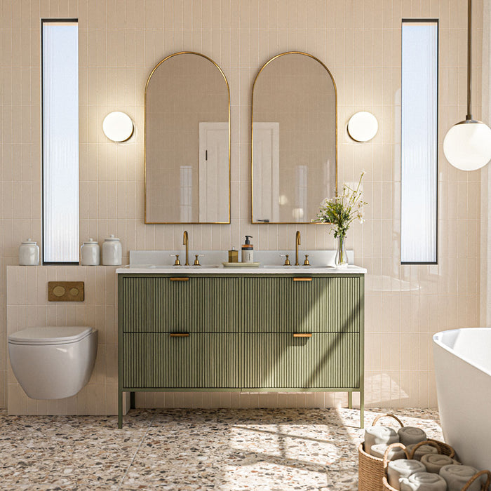 Badezimmer mit vertikal verlegten Gallery Beige Glänzenden Wandfliesen im Format 5 × 20 cm in einem sanften neutralen Farbton, kombiniert mit Bodenfliesen im Terrazzo-Stil, einem geriffelten grünen Waschtischunterschrank, Messingdetails und Rundbogenspiegeln.