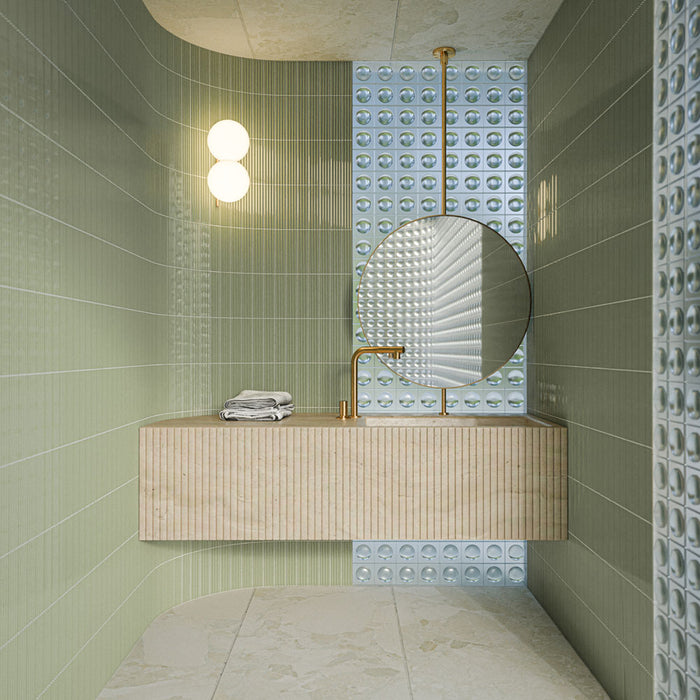 Badezimmer mit Gallery Rainfarn Grün DEKOR Glänzenden Wandfliesen im Format 5 × 20 cm, kombiniert mit strukturierten Akzentfliesen, einem schwebenden Waschtisch in Steinoptik, einem runden Spiegel und Messingarmaturen.