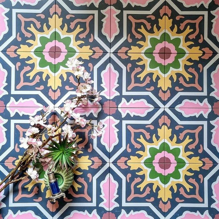 Dekoratives Interior mit Kuba Havana Feinsteinzeugfliesen im marokkanischen Stil im Format 20 × 20 cm. Das kräftige geometrische Muster in Navy-, Rosa-, Grün- und Senftönen wird mit floralen Accessoires inszeniert und unterstreicht den lebendigen, vintage-inspirierten Charakter der Fliese.