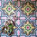 Dekoratives Interior mit Kuba Havana Feinsteinzeugfliesen im marokkanischen Stil im Format 20 × 20 cm. Das kräftige geometrische Muster in Navy-, Rosa-, Grün- und Senftönen wird mit floralen Accessoires inszeniert und unterstreicht den lebendigen, vintage-inspirierten Charakter der Fliese.