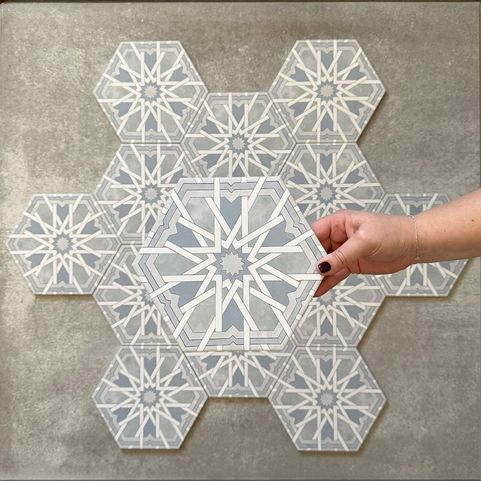 Hand hält eine sechseckige Porzellanfliese Medina Hormuz Azurblau im marokkanischen Stil (18,7 × 21,6 cm), präsentiert vor einer Gruppendarstellung, um das markante, sternförmige geometrische Muster in sanften Blau- und Weißtönen hervorzuheben.