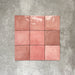 Flatlay von Zellige Rosa Quadrat Keramikfliesen im marokkanischen Stil im Format 13,2 × 13,2 cm, in sanften Blush-, Altrosa- und warmen Rosétönen. Feine Farbvariation und leicht unregelmäßige Kanten werden im schlichten Raster auf strukturiertem grauem Hintergrund präsentiert und unterstreichen die handgefertigte Zellige-Optik.