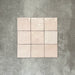 Flatlay von Zellige Rosa Nebel Quadrat Keramikfliesen im marokkanischen Stil im Format 13,2 × 13,2 cm, in sanften Rosa- und Blushtönen. Im einfachen Raster auf strukturiertem grauem Hintergrund angeordnet, um die glänzende Glasur, die dezente Farbvariation und die handgefertigte Zellige-Optik zu zeigen.