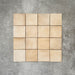 Flatlay von Zellige Sandbeige Matt Quadrat Keramikfliesen im marokkanischen Stil im Format 10 × 10 cm, in warmen Beige- und Sandtönen. Die Fliesen sind in einem schlichten Raster auf strukturiertem grauem Hintergrund angeordnet, um die feine Farbvariation und die handgefertigte Zellige-Oberfläche zu zeigen.