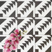 Almeira Azteca Feinsteinzeugfliesen im marokkanischen Stil, angeordnet in einem sich wiederholenden Muster, das das markante geometrische Design mit gestuften Dreiecken hervorhebt. Mit rosafarbenen Blumen kombiniert, um einen spannenden Kontrast zu schaffen, Format 20 × 20 cm.